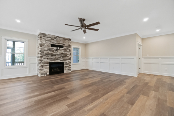 Spacious living room in new homes in Richmond with wood floors, stone fireplace, dual windows, beige walls, and a ceiling fan.