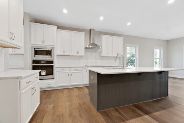 Modern kitchen in a new home with white cabinets, stainless steel appliances, a dark island, and wood flooring.