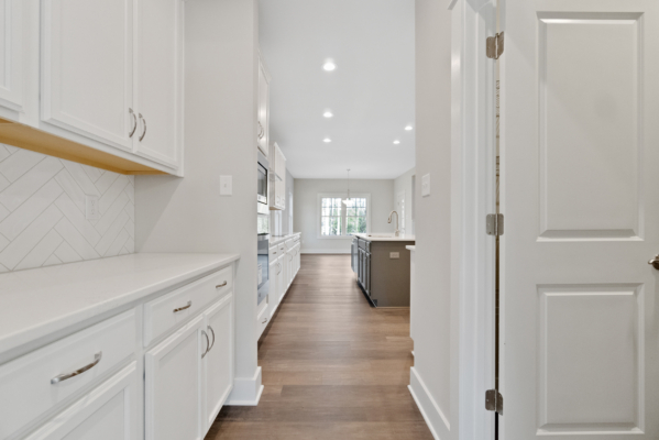 Modern kitchen with white cabinets, herringbone backsplash, and wood floors in a new home leading to a bright dining area.