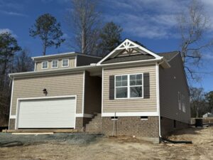 A beige two-story house in Poplar Village, with a garage, brick foundation, and white trim under a blue sky.