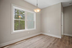 Empty room with a window, hardwood floor, and a hanging light fixture.