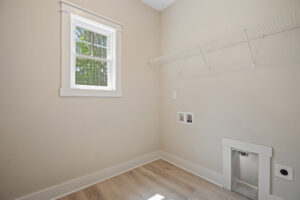 Empty laundry room with beige walls, a window, vent outlet, and wire shelf. Light wood flooring.