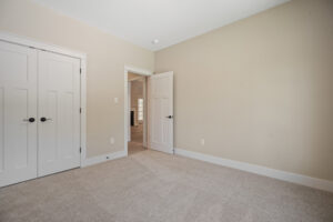Empty beige room with an open door, white closet, and carpeted floor.