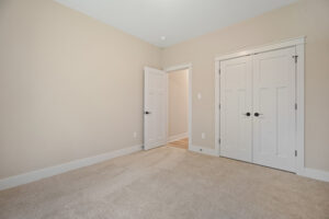 Empty beige room with carpet, white trim, open door, and double closet.