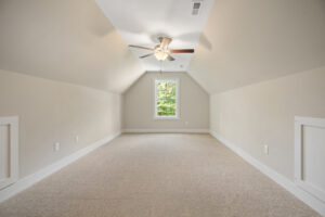 Narrow attic room with beige carpet, sloped ceiling, central window, and a ceiling fan.
