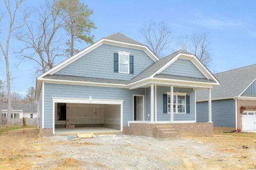 Newly constructed blue house on Lot 3 in Haley Meadows with a covered porch, open garage, and brick steps amid bare trees.