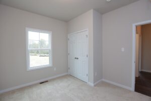 Empty room with beige carpet and gray walls—perfect for new homes in Richmond VA, featuring window, closet, and open doorway.