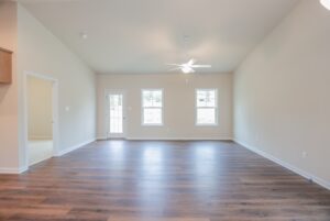 Bright, empty living room with wooden floors, beige walls, and ceiling fan found in new homes in Richmond VA.