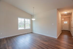 Bright empty room with wood floors in one of the stunning new homes in Richmond VA, featuring a large window and hallway.