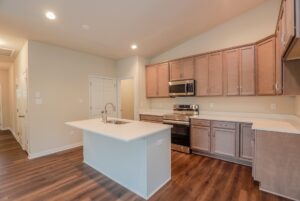 Modern kitchen in new homes in Richmond VA features wood cabinets, stainless appliances, island sink, and wood flooring.