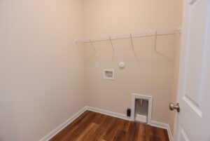 Empty laundry room in new homes in Richmond VA with beige walls, wood floor, wire shelf, and washer/dryer hookups.