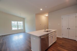 Modern kitchen in new homes in Richmond VA with white island, stainless dishwasher, and bright dining area views.