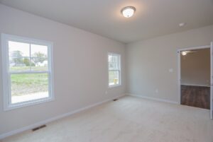 Empty carpeted room with beige walls, two windows, and open door to wood flooring—ideal for new homes in Richmond VA.