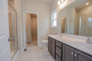 Modern bathroom in new homes in Richmond VA with double sink vanity, glass shower, large mirror, and tiled floor.