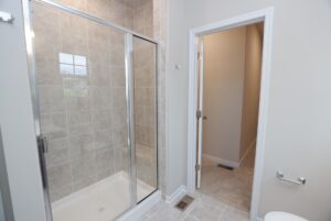 A tiled walk-in shower with glass doors, perfect for new homes in Richmond VA, sits by the bathroom entrance and hallway.