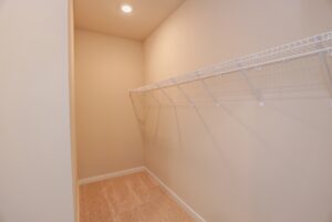 Empty walk-in closet in one of the new homes in Richmond VA, with beige walls, carpeted floor, and a white wire shelf.