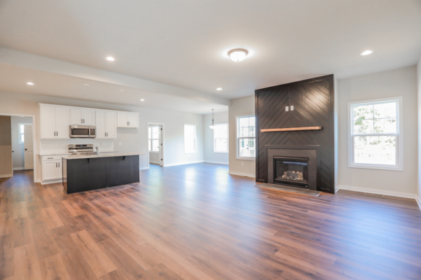 Spacious modern living room with hardwood floors, a black accent wall with fireplace, and an open kitchen like a photo gallery.