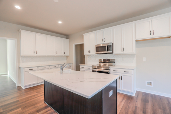 Modern kitchen with white cabinets, stainless steel appliances, a large island with marble countertop, and photo gallery walls.