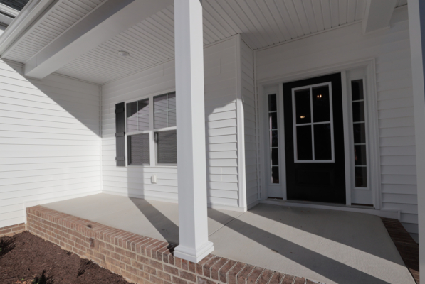 A white house porch with a black door, glass panels, and brick steps casts artful shadows in this photo gallery.