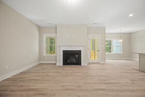 Spacious room with light wood flooring, a white fireplace, and windows near a glass door leading outside.