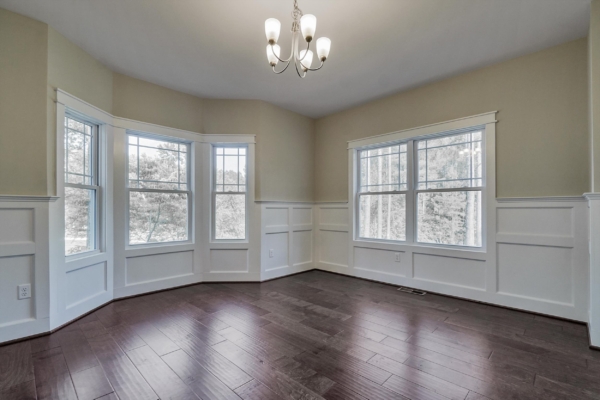 Bright room with chandelier, large bay windows, and dark wood flooring. Cream walls with white wainscoting.