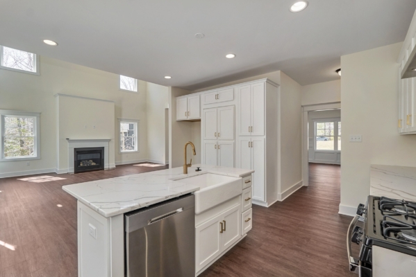 Modern kitchen with white cabinets, marble countertops, stainless steel appliances, and a view of a living area with fireplace.