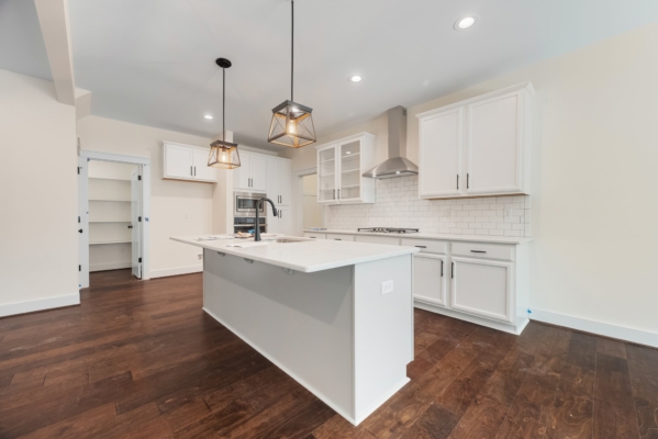 Modern kitchen with white cabinets, island, pendant lights, and wooden floor. Open pantry door visible.