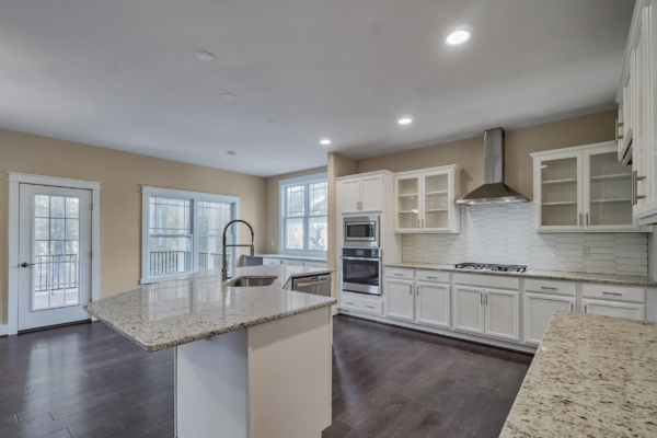 Modern kitchen with island, granite countertops, white cabinets, stainless steel appliances, and dark wood flooring.