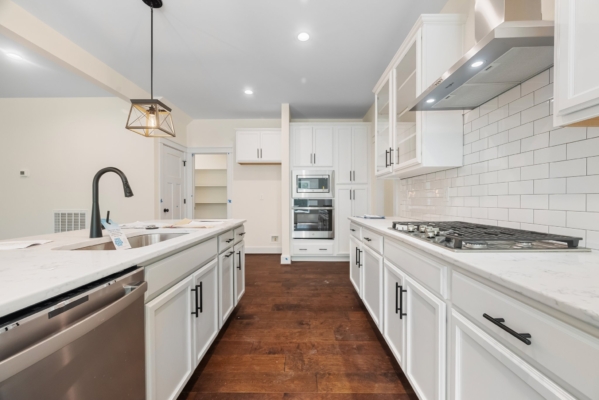Modern kitchen with white cabinets, stainless steel appliances, wooden floor, and a large island with pendant light.