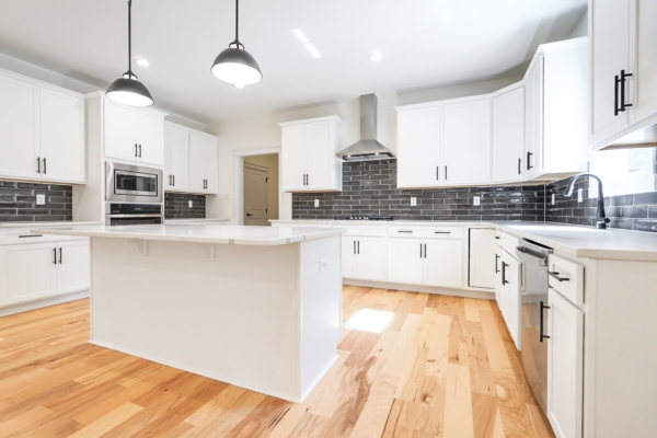 Bright white kitchen with wood floors, black tile backsplash, island, and stainless steel appliances.