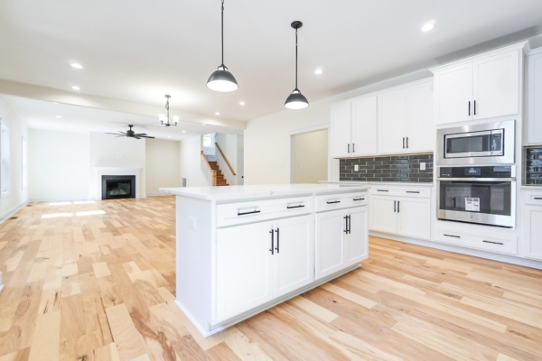 Modern kitchen with white cabinets, island, stainless steel appliances, and bright hardwood floors, adjacent to living area.