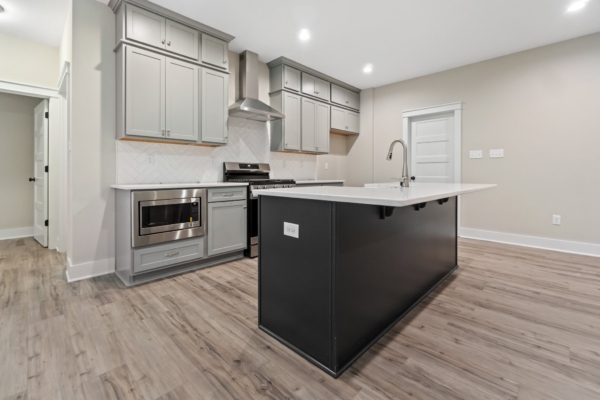 Modern kitchen with gray cabinets, island with sink, stainless steel appliances, and wood flooring.