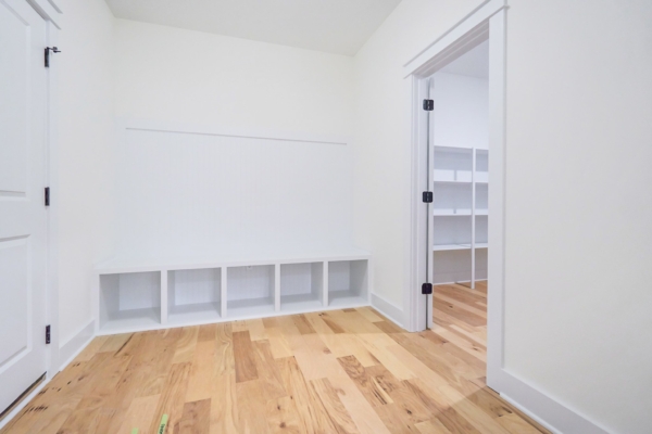Minimalist room with light wood flooring, storage cubbies, and a doorway leading to a room with more shelves.