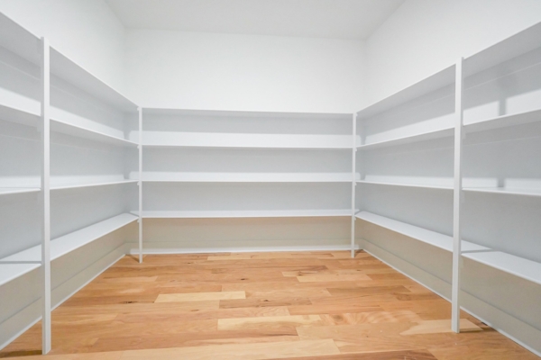 Empty white shelving in a walk-in pantry with wooden floors.
