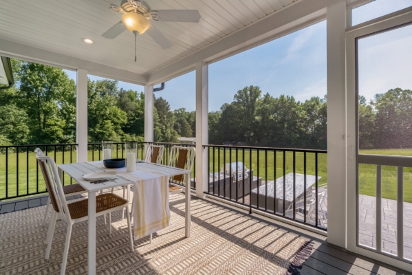 Outdoor patio with white dining table, chairs, ceiling fan, and view of green lawn and trees.