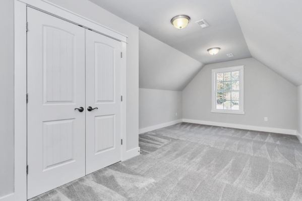 Attic room with gray carpet, closed double doors, and a window. White walls and ceiling lights.
