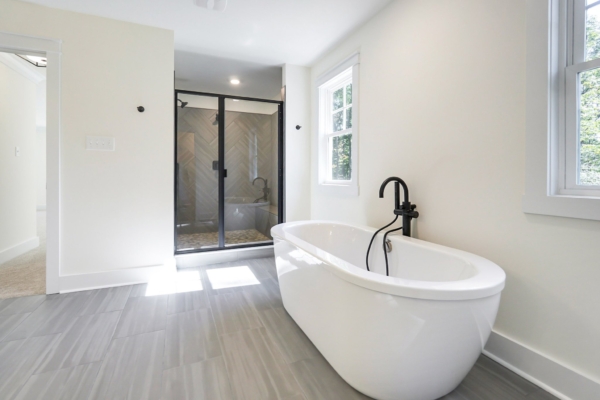 Minimalist bathroom with a freestanding white tub, black faucet, and a glass-enclosed shower. Light gray tiled floor.