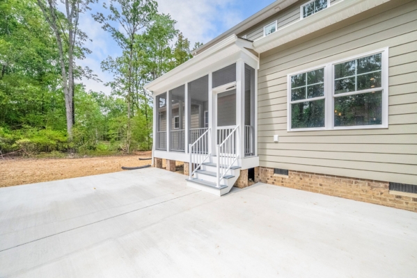 Backyard view of a house with a screened porch, steps, and a concrete patio, surrounded by trees.