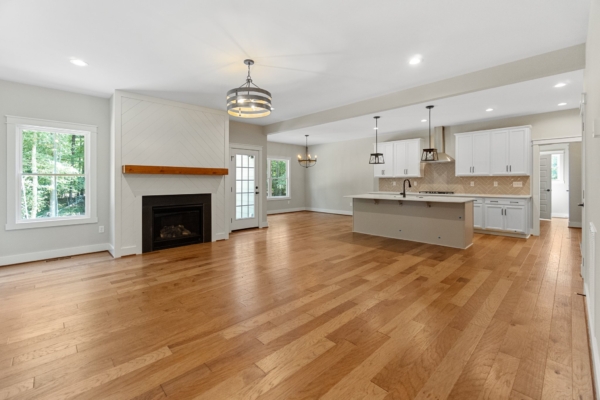 Open-concept living area with hardwood floors, kitchen island, fireplace, and large windows.
