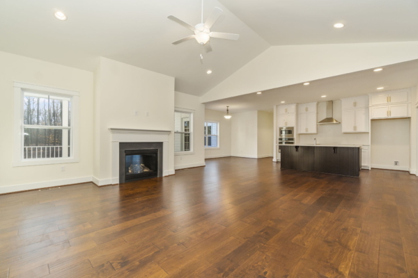 Spacious room with hardwood floors, white walls, fireplace, ceiling fan, and modern kitchen with island.