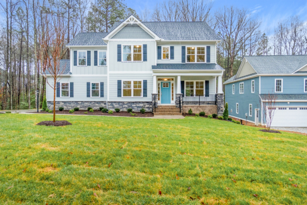 Two-story house with gray siding, blue shutters, and a large front lawn, surrounded by trees.