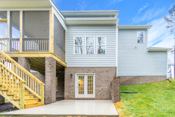 Side view of a modern house with brick and siding, featuring a screened porch and wooden stairs leading to a patio.