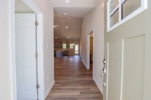 Open front door revealing a bright hallway with wooden floors leading to a spacious living area.