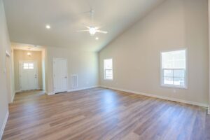 Spacious empty room with wooden floor, two windows, white door, and ceiling fan.