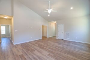 Spacious empty living room with wood flooring, white walls, ceiling fan, and multiple doorways.