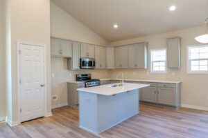 Modern kitchen with light gray cabinets, island with sink, stainless steel appliances, and wood flooring.