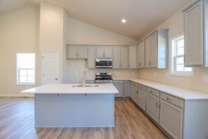 Modern kitchen with gray cabinets, a central island, stainless steel appliances, and wood flooring.