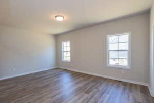 Empty room with light wood flooring, light gray walls, and two windows. Ceiling light is turned on.