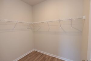 Empty walk-in closet with white wire shelving on beige walls and wooden floor.