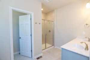 A bathroom with a glass shower, white countertop with dual sinks, and an open door.